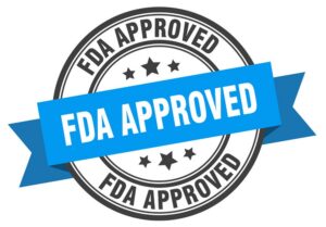 A round badge with a blue ribbon across the middle, containing the text "FDA APPROVED" in bold white letters. The border of the badge also includes "FDA APPROVED" repeatedly, with five black stars in the center background. Ideal for gummy manufacturing equipment or a gummy depositor label.