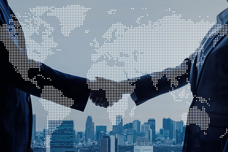 Two individuals in business attire shake hands, with a stylized world map overlay and a cityscape in the background, symbolizing a global business agreement—perhaps even finalizing the acquisition of gummy manufacturing equipment.