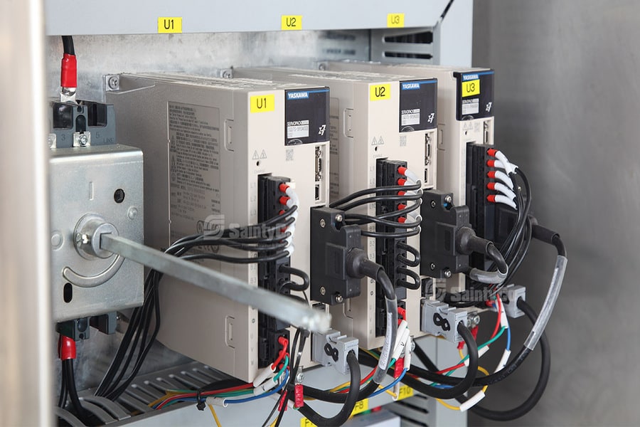 The image shows the inside of an electrical control panel with three Toshiba variable frequency drives (VFDs) labeled U1, U2, and U3, commonly used in gummy making machines. Various colored wires and connectors are attached, and the setup is mounted on a metal frame.