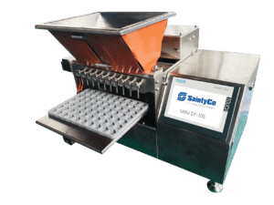 A stainless steel gummy depositor with a touchscreen display labeled "SaintyCo MINI DP-10S." The machine has a large hopper at the top and a tray with multiple tablet molds below, designed for precise gummy manufacturing.