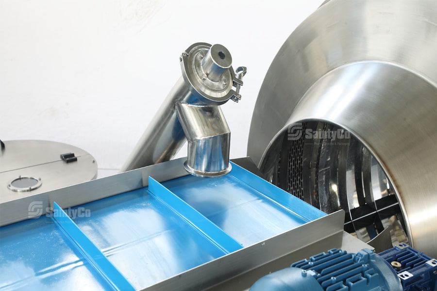 A close-up of a gummy making machine, featuring shiny stainless steel components and a blue conveyor belt. The setup includes cylindrical and rectangular metal parts, with some SaintyCo branding visible on the equipment. Everything appears to be well-maintained and clean.