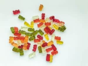 A scattered pile of colorful gummy bears, created with a Gummygenix depositor, is spread out on a white surface. These SaintyCo gummy bears come in various colors, including red, green, yellow, orange, and clear.