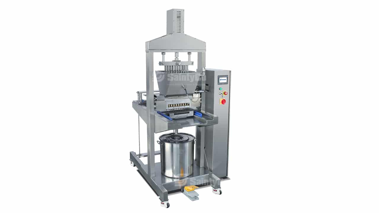 A stainless steel industrial machine, the Gummygenix features a control panel with various buttons and a digital display. It includes a conveyor system, a metal cylinder below a pressing mechanism, and a safety enclosure. The Gummygenix is used for automated processes in manufacturing gummies.