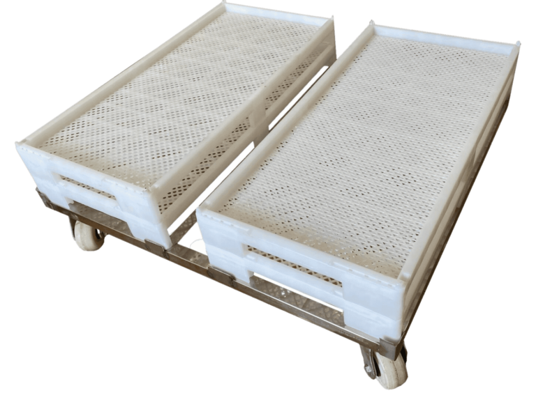 A metal trolley with four caster wheels holds two large, perforated white plastic trays designed for gummy manufacturing equipment. The trays have handles on the shorter sides for ease of carrying and feature a textured surface with small holes for ventilation or drainage.