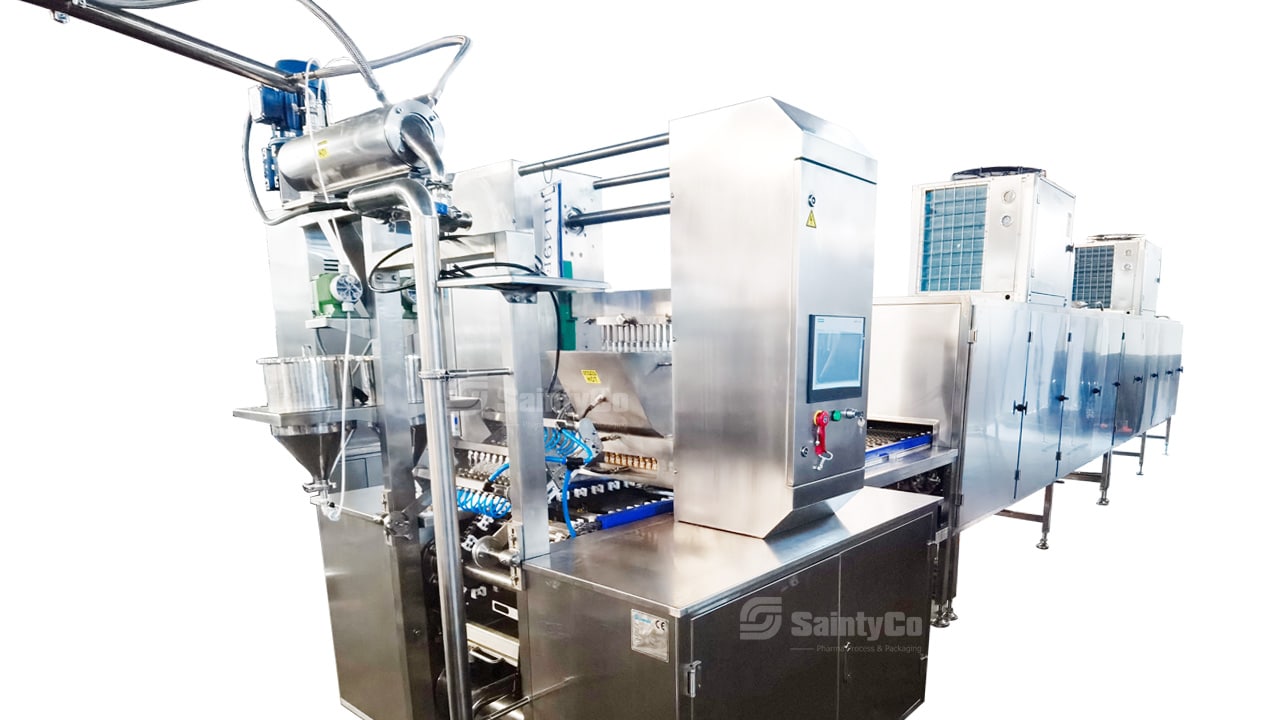 The SaintyCo stainless steel automated production line machine, ideal for pharmaceutical or food processing industries, features compartments, a control unit with a screen, pipelines, and other mechanical components. Perfect as gummy making equipment, it ensures efficient and reliable production processes.