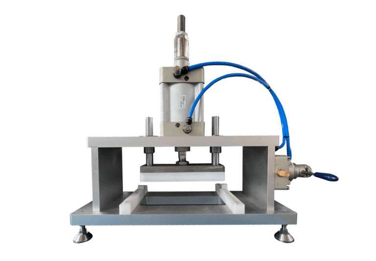 Image of an industrial gummy making machine with metal components and blue hoses, placed on a flat base. The machine appears designed for pressing, molding, or stamping materials like gummies, featuring adjustable screws and a cylindrical actuator.