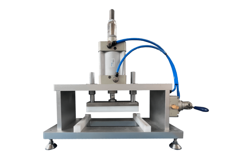 Image of an industrial gummy making machine with metal components and blue hoses, placed on a flat base. The machine appears designed for pressing, molding, or stamping materials like gummies, featuring adjustable screws and a cylindrical actuator.