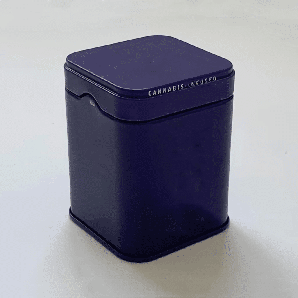 A dark blue rectangular tin container with a fitted lid. The container boasts the words "Cannabis-Infused" in white along the top edge. Its surface is smooth and shiny, with minimal design elements, photographed against a plain white background.