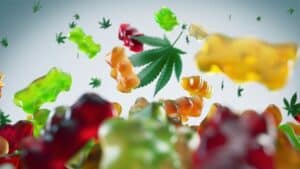 An assortment of colorful gummy bears is thrown into the air, with a cannabis leaf among them. The gummies and the leaf are suspended mid-air, appearing vibrant and dynamic against a plain background—a testament to Gummygenix and their state-of-the-art gummy manufacturing equipment.