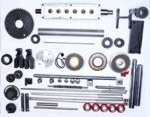 An assortment of mechanical parts for the gummy making machine is arranged on a white background. Items include gears, shafts, rods, bearings, fasteners, and various components of differing sizes and shapes, each organized neatly in rows. The components appear to be for industrial machinery.