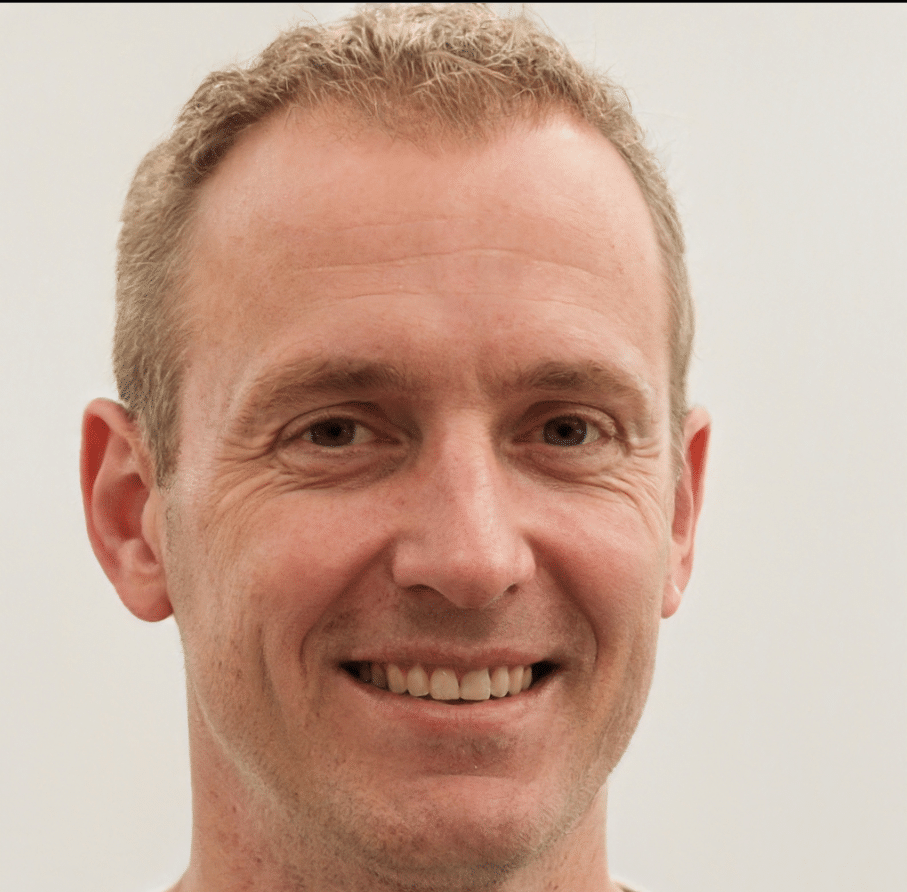 A middle-aged man with short, light brown hair and a friendly smile is facing the camera. He has a fair complexion and is wearing a white shirt. The background is plain and light-colored, creating an inviting contact for viewers.