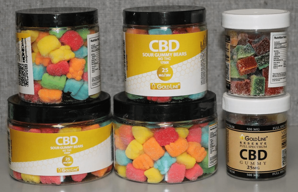 Five jars of GoldLine CBD gummies, including two labeled "GoldLine CBD Sour Gummy Bears" with multicolored gummies, and three labeled "GoldLine Reserve CBD Gummy Full Spectrum" featuring mixed color gummies. Each jar showcases various dosages and contents—a testament to the precision of gummy making machines.