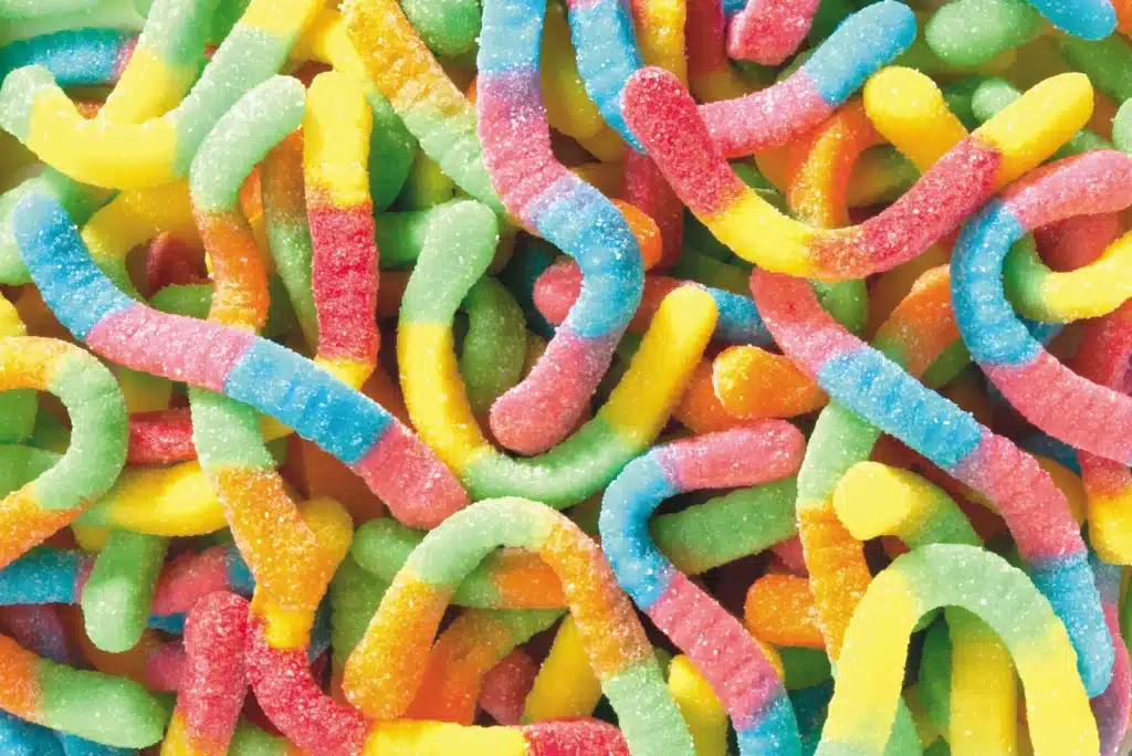 A close-up of colorful gummy worms covered in sugar. The candies are twisted and intertwined, with vibrant shades of yellow, red, green, blue, and orange.