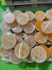 Buckets filled with orange-colored liquid and bubbles, possibly containing small orange spheres, are stacked on wooden pallets against a green floor.