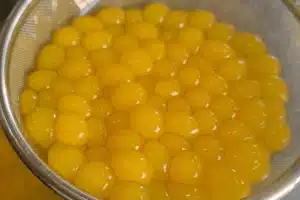 Bright yellow tapioca pearls, crafted with the GummyGenix popping boba maker, are clustered together in SaintyCo metal mesh strainer, glistening under the light.