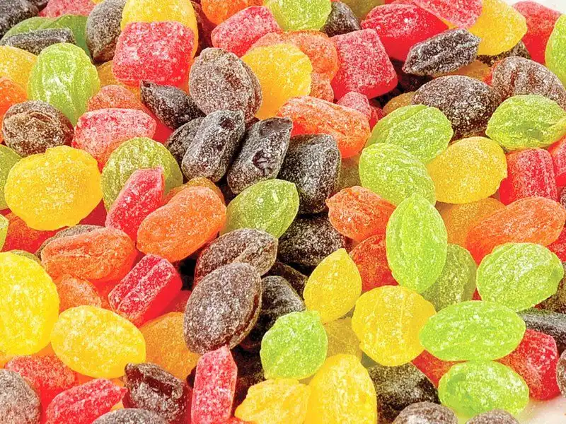 A close-up view of assorted hard candies in various shapes and bright colors, including red, yellow, green, and orange, all coated with a light dusting of sugar.