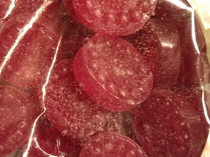 Close-up of several round, red, hard candies inside a clear plastic bag, with a sugary coating visible on the surface of the sweets.