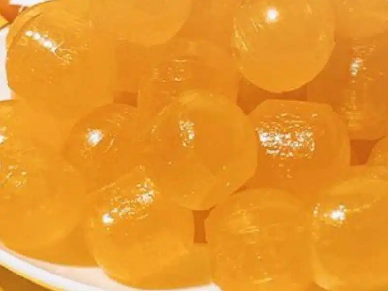 A close-up of several shiny, round, yellow-orange hard candies piled on a white plate.