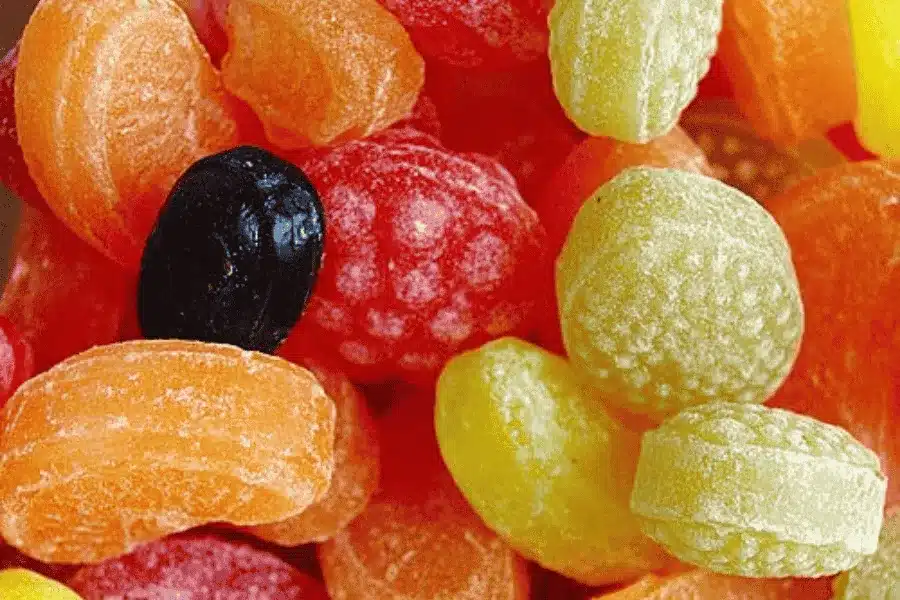 A close-up view of assorted colorful hard candies, including orange, yellow, red, and a single black piece, all with a shiny, textured surface.
